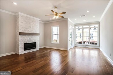 Large light filled living room with a ceiling fan, dark wood-style floors, ornamental molding, a stone fireplace opens up to a nice sunroom.