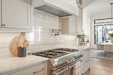 The quartzite Perla Ventana extends to the backsplash with a pot filler over the Thermador range. To the left of the range is a double drawer beverage center.
