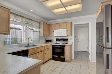 Kitchen with white microwave, freestanding refrigerator, gas stove, light brown cabinets, and crown molding