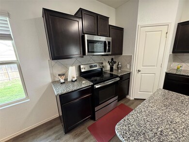 Kitchen featuring a textured wall, stainless steel appliances, light stone counters, and dark wood finished floors