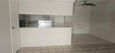 Kitchen with stainless steel stove, black microwave, light tile patterned flooring, a ceiling fan, and light countertops
