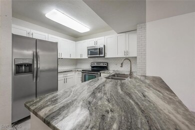 Kitchen with appliances with stainless steel finishes, light stone counters, backsplash, white cabinetry, and a textured ceiling
