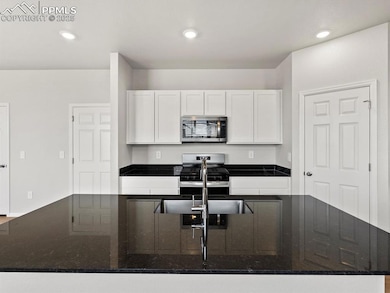 Kitchen with dark stone countertops, appliances with stainless steel finishes, white cabinets, recessed lighting, and an island with sink