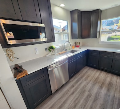 Kitchen with stainless steel appliances, light wood-style floors, and light stone counters
