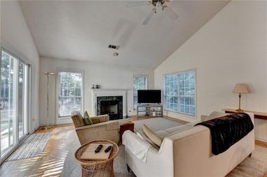Living area featuring a fireplace, ceiling fan, wood finished floors, and high vaulted ceiling