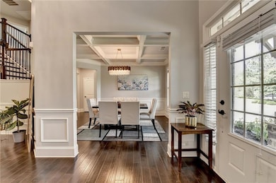 Foyer entrance with coffered ceiling, a chandelier, beamed ceiling, dark wood-style floors, and plenty of natural light