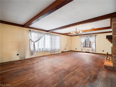 Unfurnished living room featuring a notable chandelier, beam ceiling, dark wood-type flooring, and brick wall