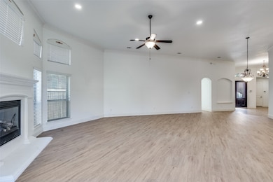 Unfurnished living room with light wood-type flooring, a glass covered fireplace, arched walkways, ceiling fan, and crown molding