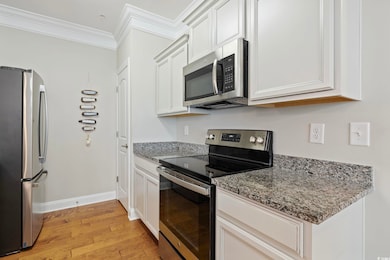 Kitchen featuring appliances with stainless steel finishes, light wood-style flooring, ornamental molding, stone counters, and white cabinets