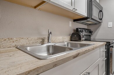 Kitchen with black range with electric cooktop, light countertops, white cabinets, and a textured wall