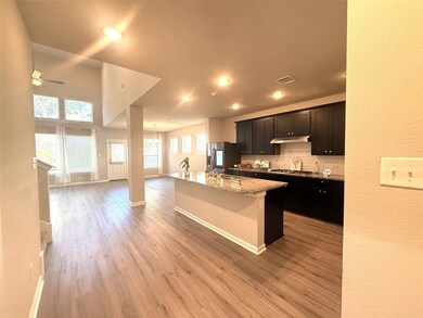 Kitchen with dark cabinetry, a center island with sink, open floor plan, light wood finished floors, and tasteful backsplash