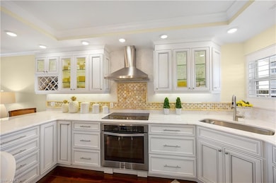 Kitchen featuring white cabinetry, ornamental molding, recessed lighting, wall chimney exhaust hood, and oven