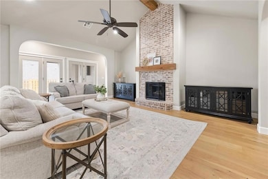 Living area featuring a ceiling fan, wood finished floors, a fireplace, arched walkways, and beamed ceiling