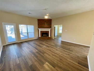 Unfurnished living room featuring a textured ceiling, a brick fireplace, dark wood finished floors, and a ceiling fan