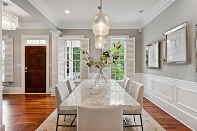 Dining space with healthy amount of natural light, dark wood-style flooring, a wainscoted wall, ornamental molding, and a chandelier
