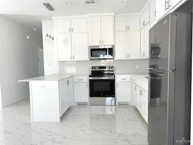 Kitchen featuring backsplash, stainless steel appliances, a peninsula, light marble finish flooring, and white cabinets