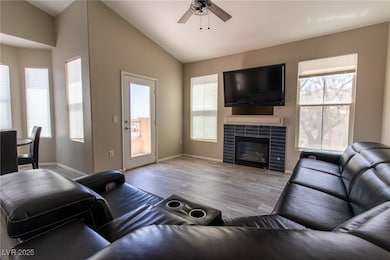 Living room with light wood-type flooring, lofted ceiling, plenty of natural light, and a tiled fireplace