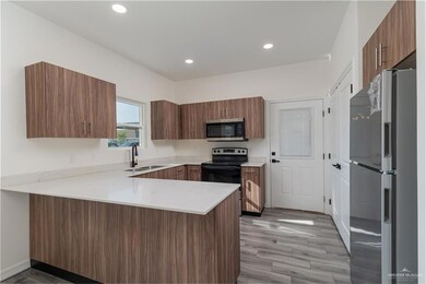 Kitchen featuring a sink, light countertops, stainless steel microwave, a peninsula, and freestanding refrigerator