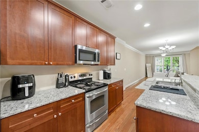 Kitchen featuring appliances with stainless steel finishes, light wood-type flooring, crown molding, light stone counters, and a chandelier