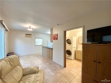 Tiled living room featuring stacked washer and clothes dryer and an AC wall unit