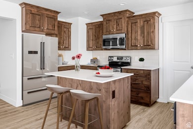 Kitchen featuring light wood finished floors, stainless steel appliances, backsplash, a kitchen island, and light countertops