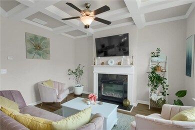 Living area featuring coffered ceiling, wood finished floors, beamed ceiling, a glass covered fireplace, and a ceiling fan