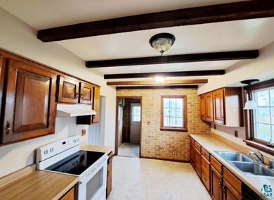 Kitchen with beam ceiling, range, sink, and brick 