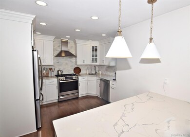 Kitchen with white cabinets, appliances with stainless steel finishes, wall chimney exhaust hood, hanging light fixtures, and light stone countertops