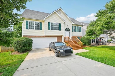 Raised ranch featuring driveway, brick siding, an attached garage, and a front yard