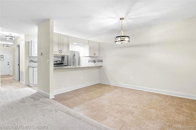 Kitchen with decorative backsplash, hanging light fixtures, a peninsula, a chandelier, and freestanding refrigerator