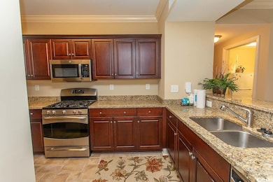 Kitchen featuring stainless steel appliances, a sink, ornamental molding, and light stone counters