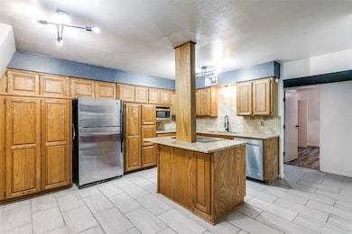 Kitchen featuring appliances with stainless steel finishes, a center island, light stone countertops, backsplash, and wood finish floors