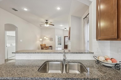 Kitchen with arched walkways, dark stone counters, ceiling fan, a peninsula, and recessed lighting