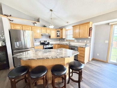Kitchen with stainless steel appliances, under cabinet range hood, lofted ceiling, light wood-style floors, and a breakfast bar area