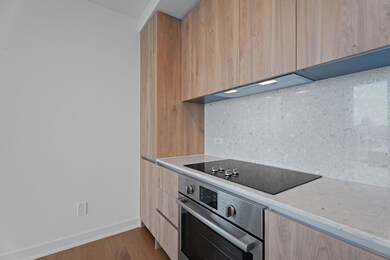 Kitchen with oven, modern cabinets, black electric stovetop, light brown cabinets, and backsplash