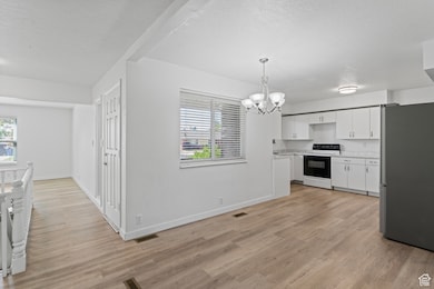 Kitchen featuring freestanding refrigerator, white cabinetry, electric range, light countertops, and a chandelier
