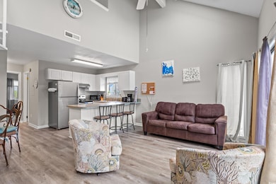 Living room featuring ceiling fan, light wood-type flooring, a towering ceiling, visible vents, and baseboards