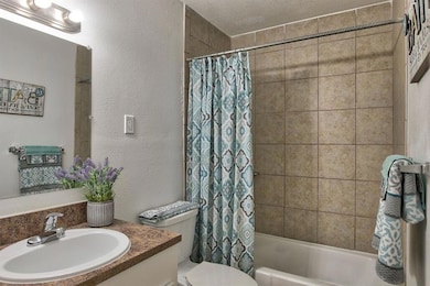 Full bathroom with vanity, toilet, shower / bathtub combination with curtain, and a textured ceiling