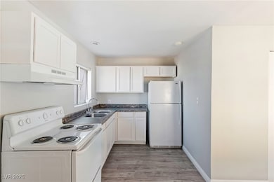 Kitchen with white appliances, dark countertops, white cabinets, light wood-style flooring, and under cabinet range hood