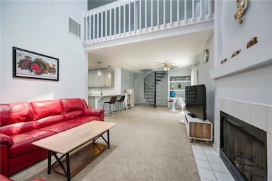 Living area featuring a tiled fireplace, light carpet, a towering ceiling, ceiling fan, and stairway