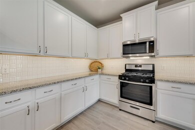 Kitchen featuring light stone counters, stainless steel appliances, tasteful backsplash, and white cabinetry