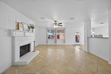 Unfurnished living room with light tile patterned floors, a ceiling fan, a brick fireplace, and a textured ceiling
