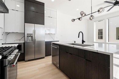 Kitchen featuring white cabinets, modern cabinets, range hood, stainless steel appliances, and a sink