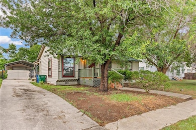 View of property hidden behind natural elements with a detached carport, a porch, and concrete driveway