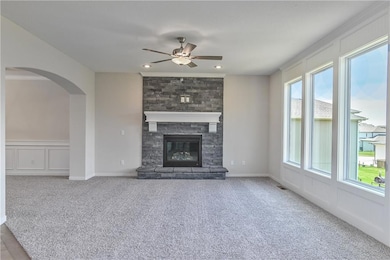 Unfurnished living room featuring a ceiling fan, carpet, a decorative wall, arched walkways, and a fireplace