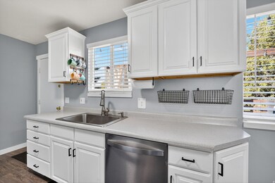 Kitchen with stainless steel dishwasher, light countertops, white cabinets, and dark wood-type flooring.
