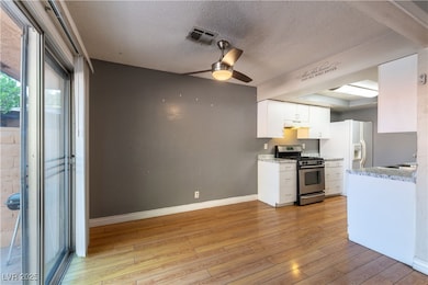 Kitchen featuring stainless steel gas stove, white cabinets, light wood-style floors, ceiling fan, and a textured ceiling