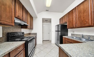Kitchen featuring black electric range oven, backsplash, stainless steel refrigerator, sink, and light tile floors
