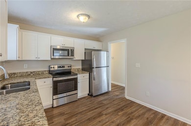 Kitchen with light stone counters, dark wood-style flooring, appliances with stainless steel finishes, white cabinets, and a sink