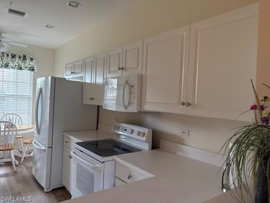 Kitchen featuring white appliances, white cabinets, light countertops, light wood-style flooring, and recessed lighting